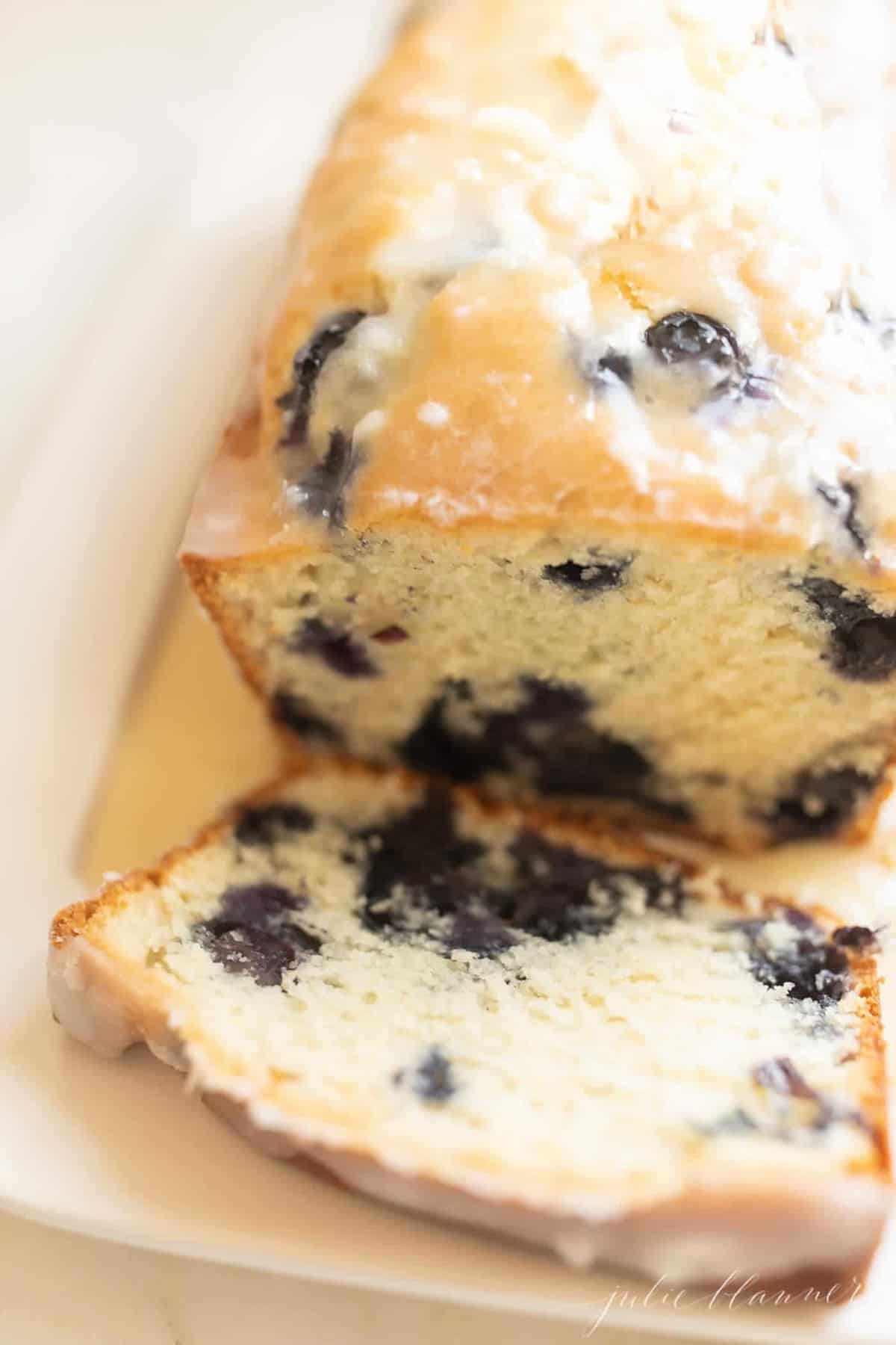 A white platter with a loaf of blueberry bread with a lemon glaze.