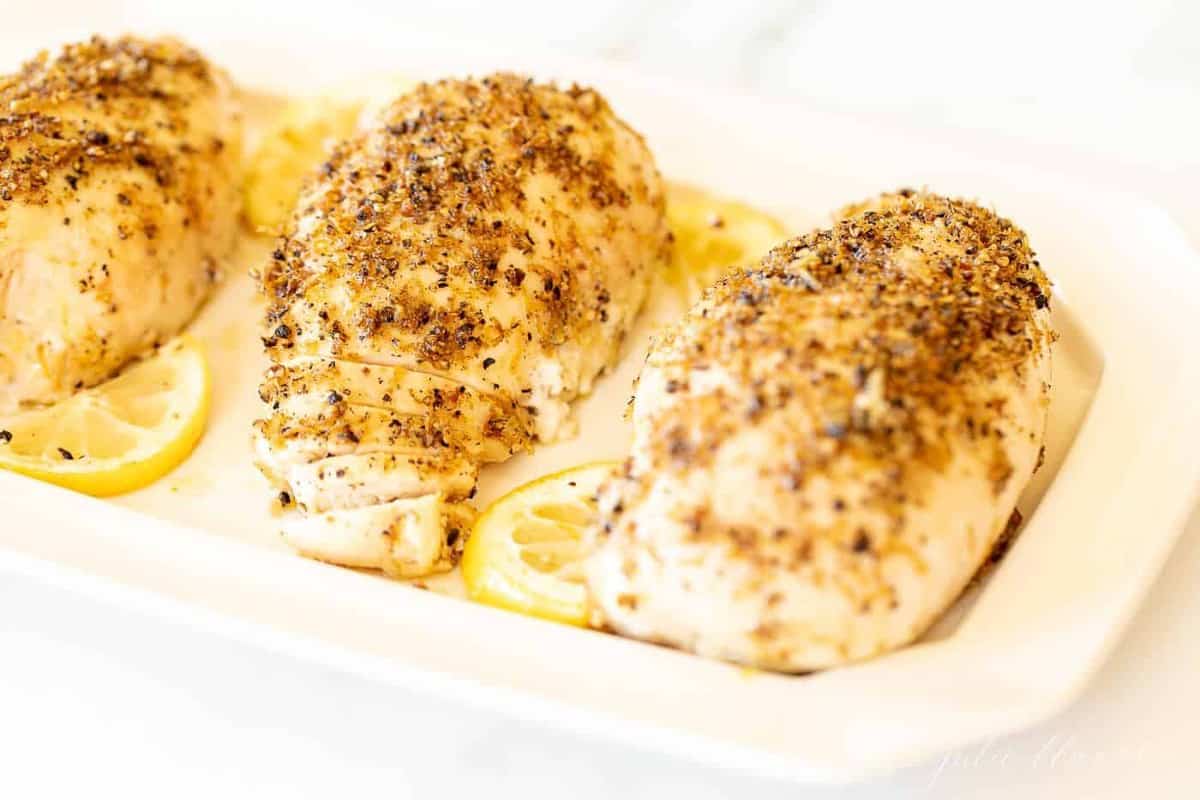 A white tray with a recipe for lemon pepper chicken and slices of lemon.