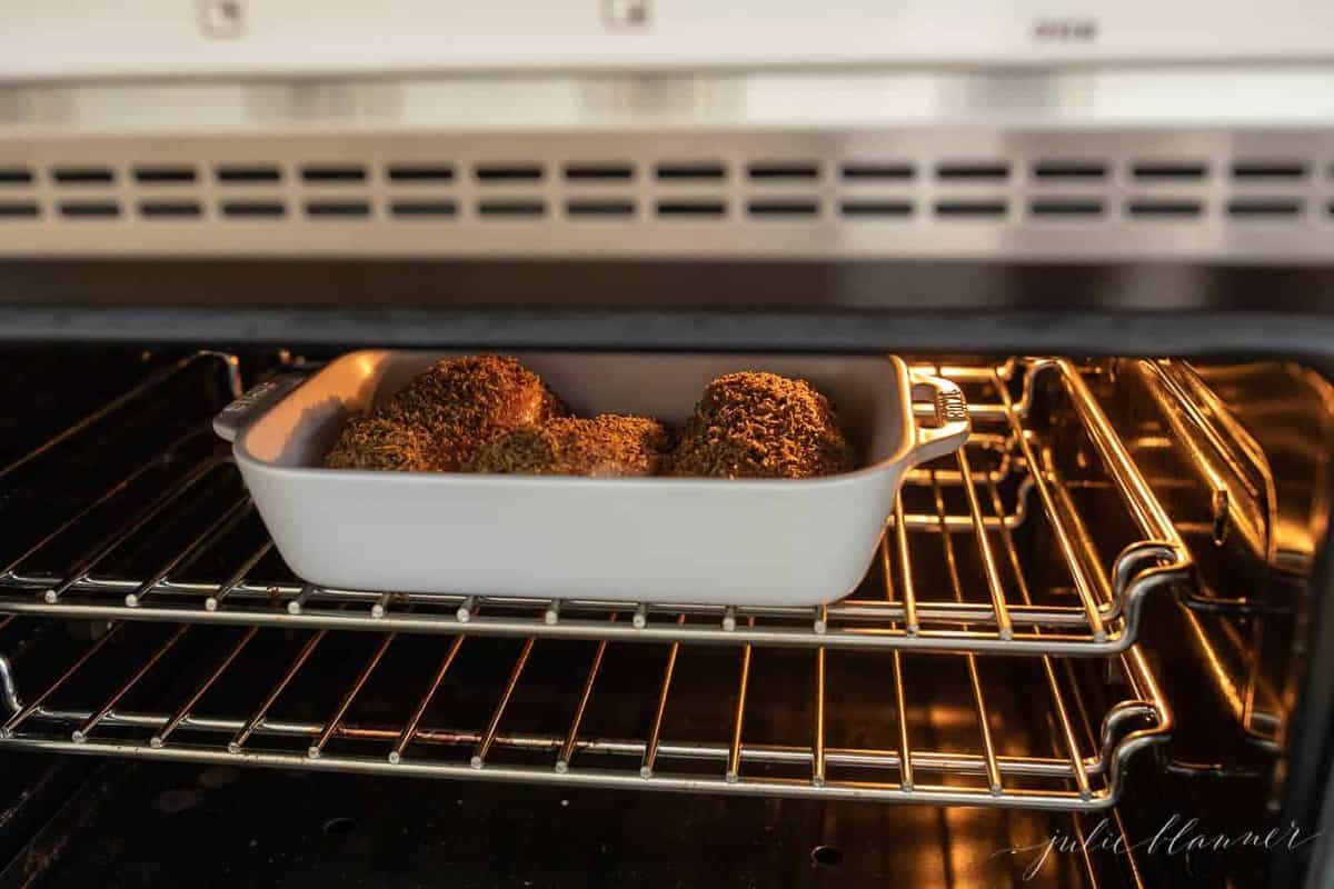 A white baking dish in an oven, filled with lemon pepper baked chicken.