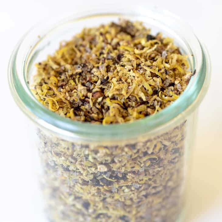 A glass jar on a marble surface, filled with lemon pepper seasoning blend.