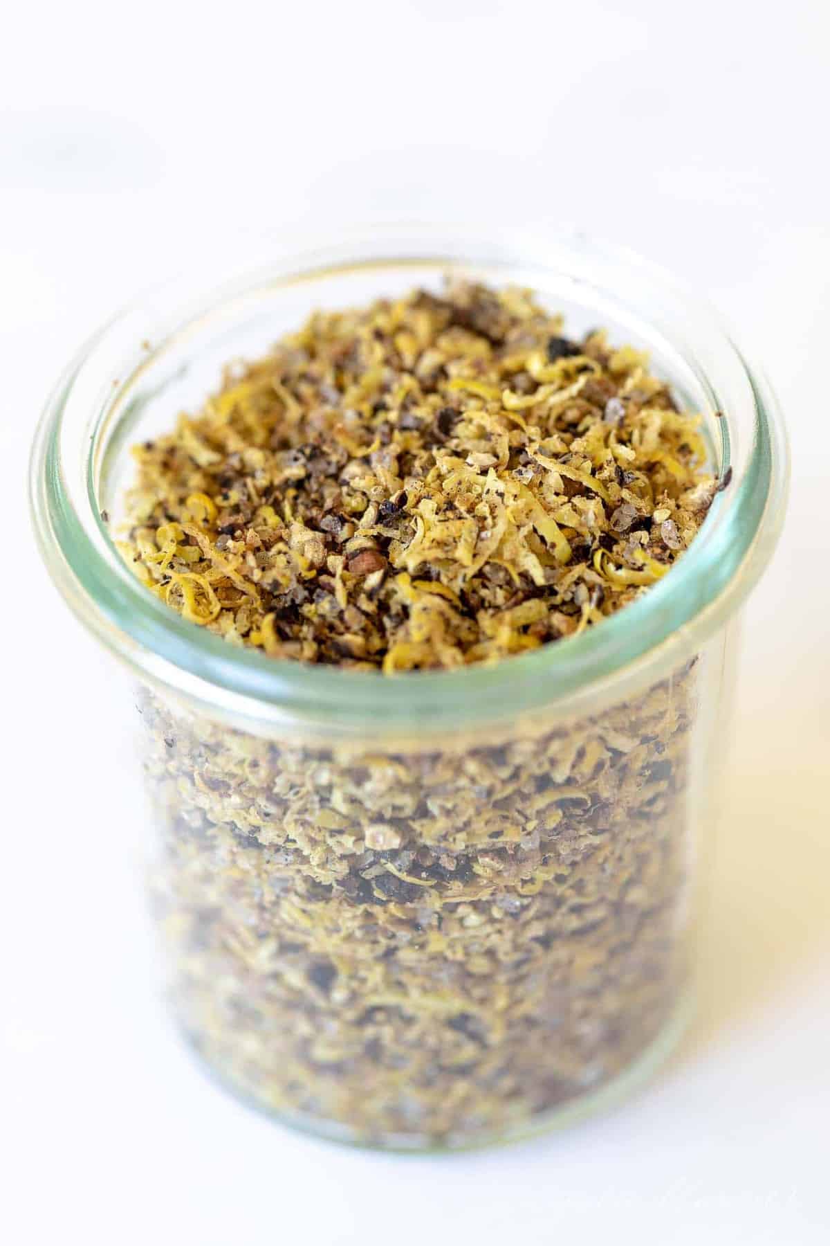 A glass jar on a marble surface, filled with lemon pepper seasoning blend.