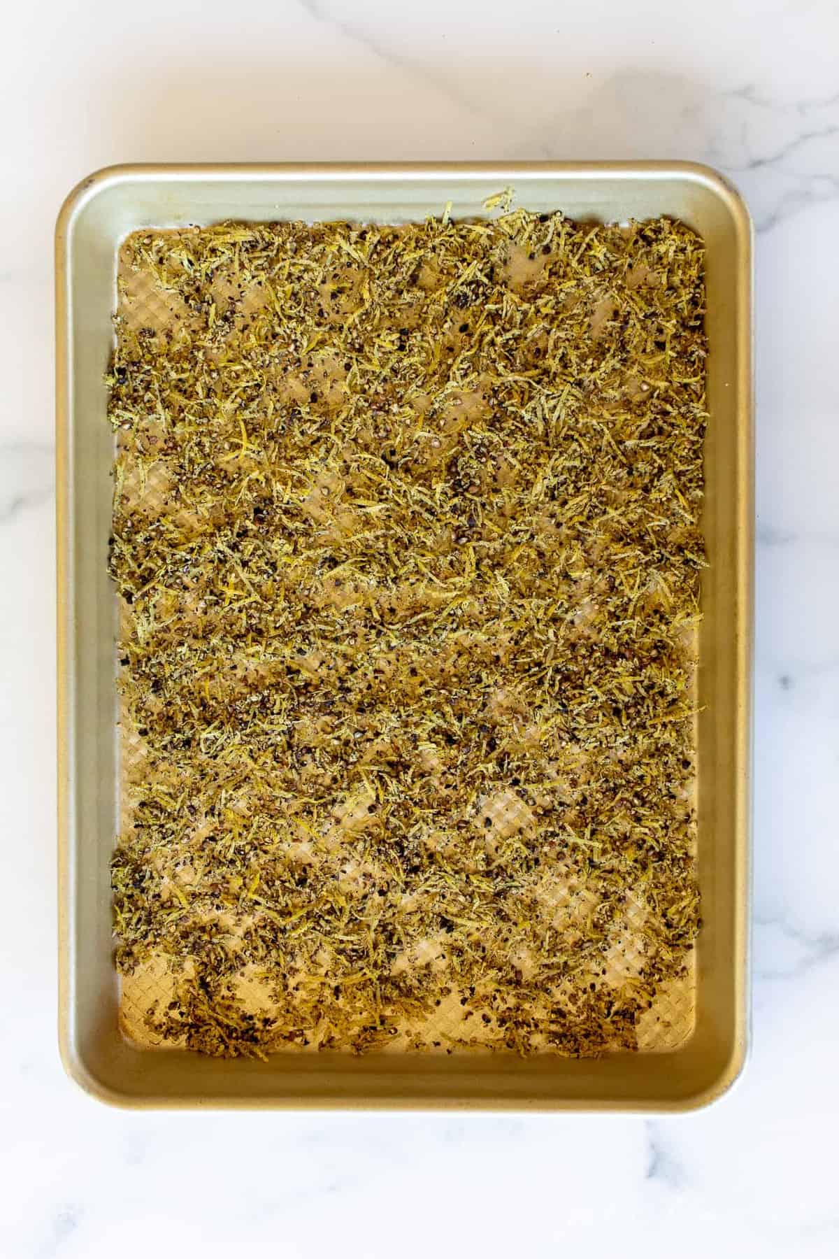 A gold sheetpan filled with baked lemon pepper seasoning.