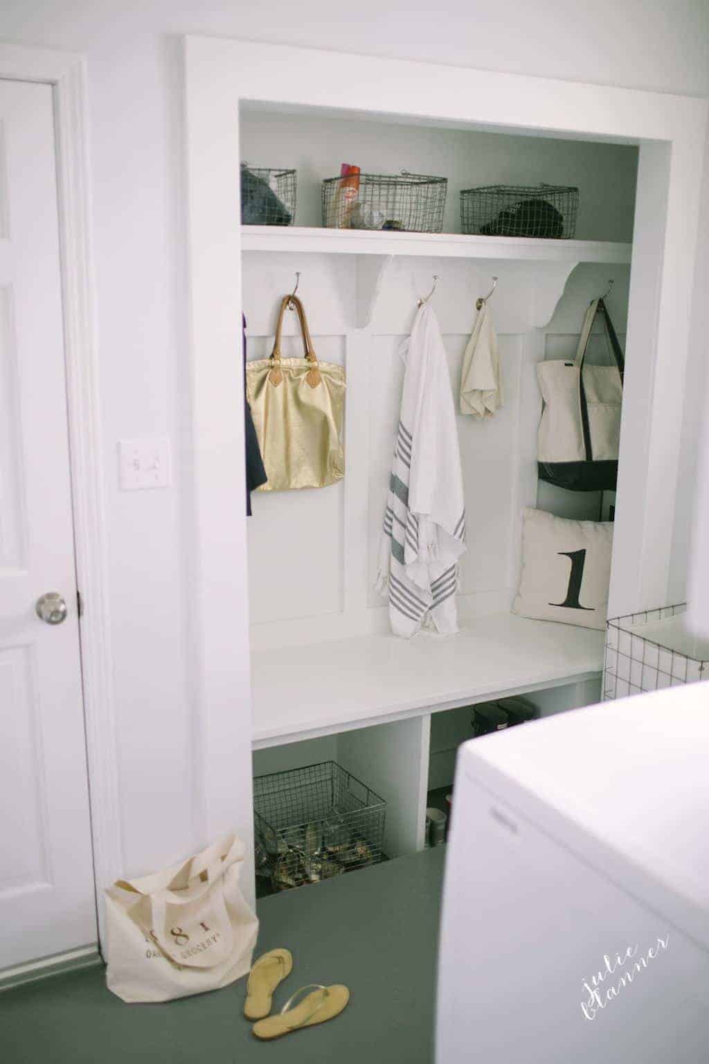 A look into a mudroom with baskets and coats hanging from farmhouse hooks.