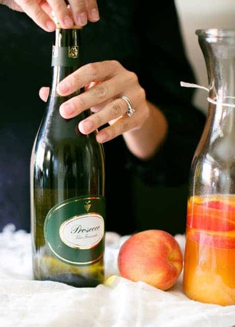 A bottle of Prosecco next to a peach and a glass carafe.
