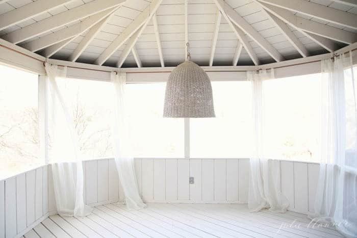 A screened in porch painted with beige paint and sheer curtains