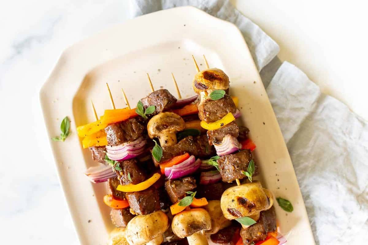 A white platter filled with grilled steak kabobs.