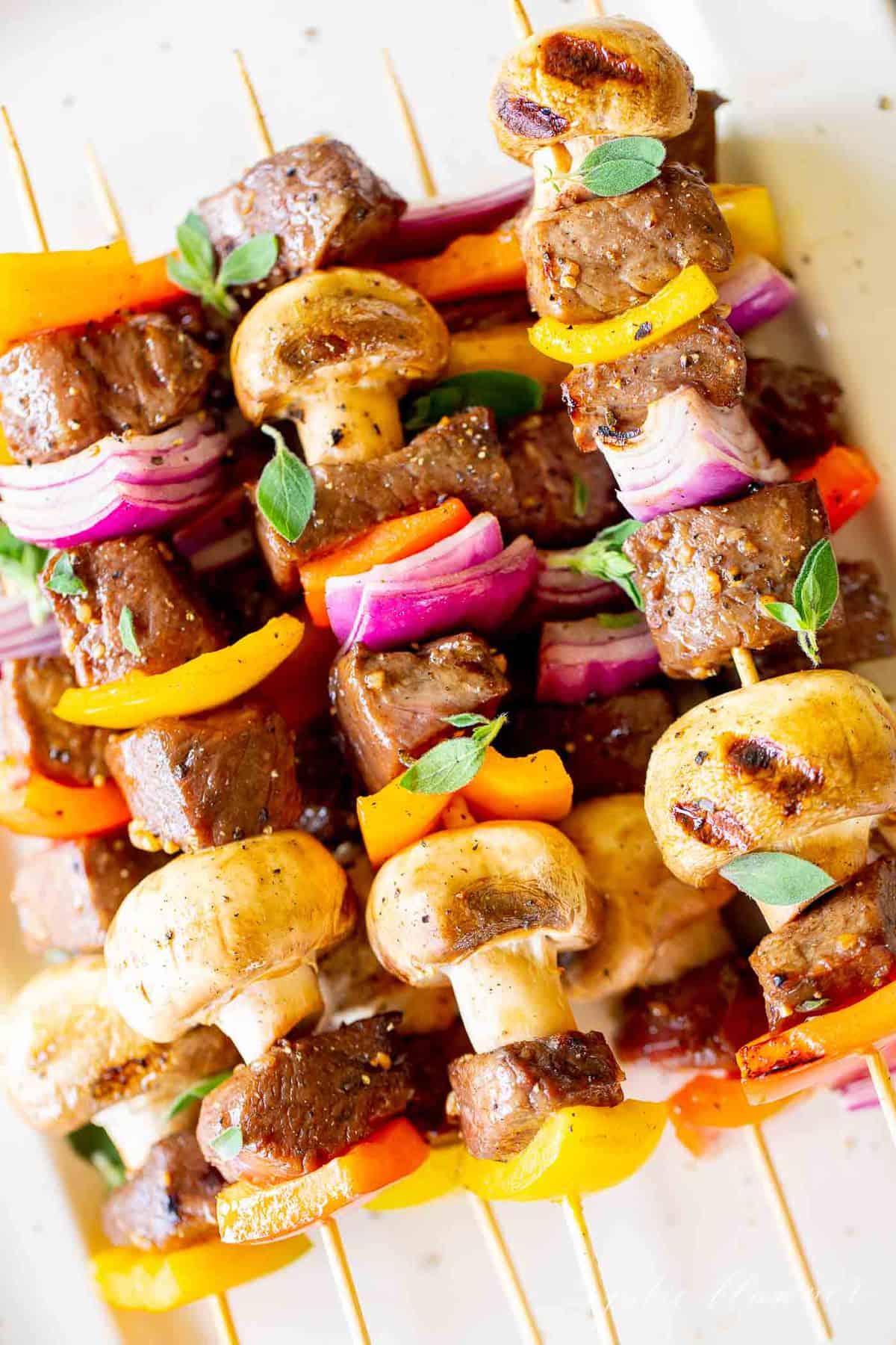 A close up image of steak kabobs on a white platter.