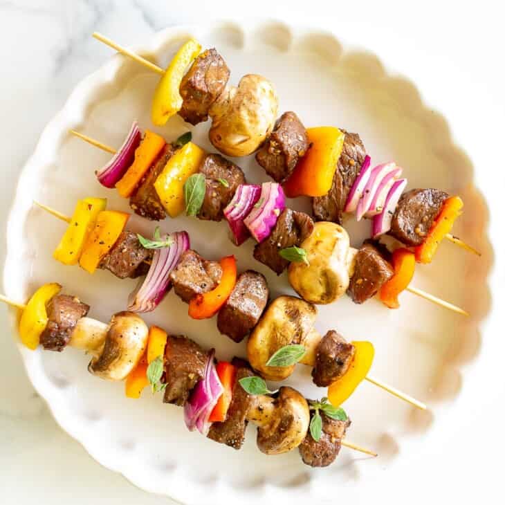 A white platter filled with grilled steak kabobs.