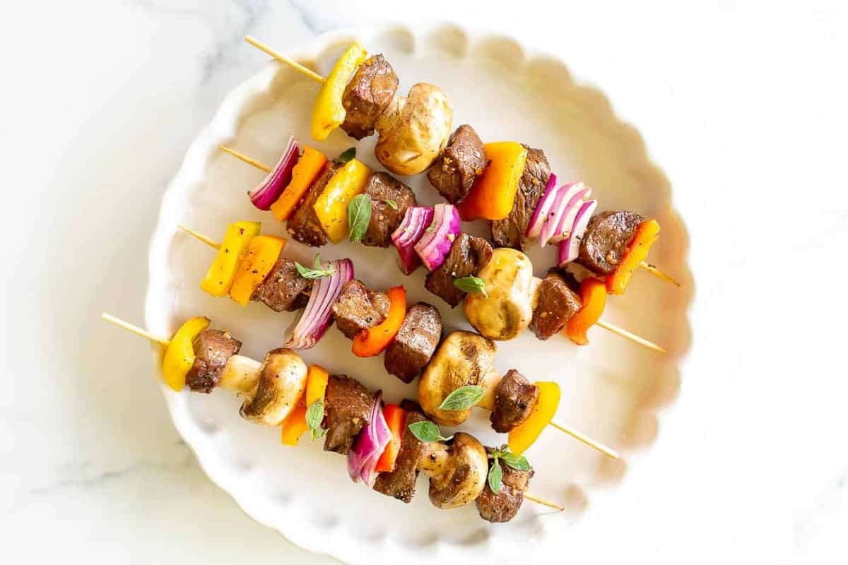 A white platter filled with grilled steak kabobs.