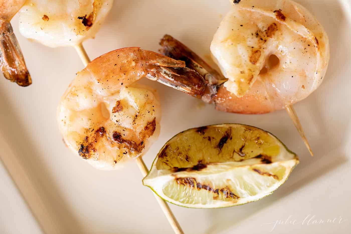 close up of white platter filled with grilled shrimp skewers.