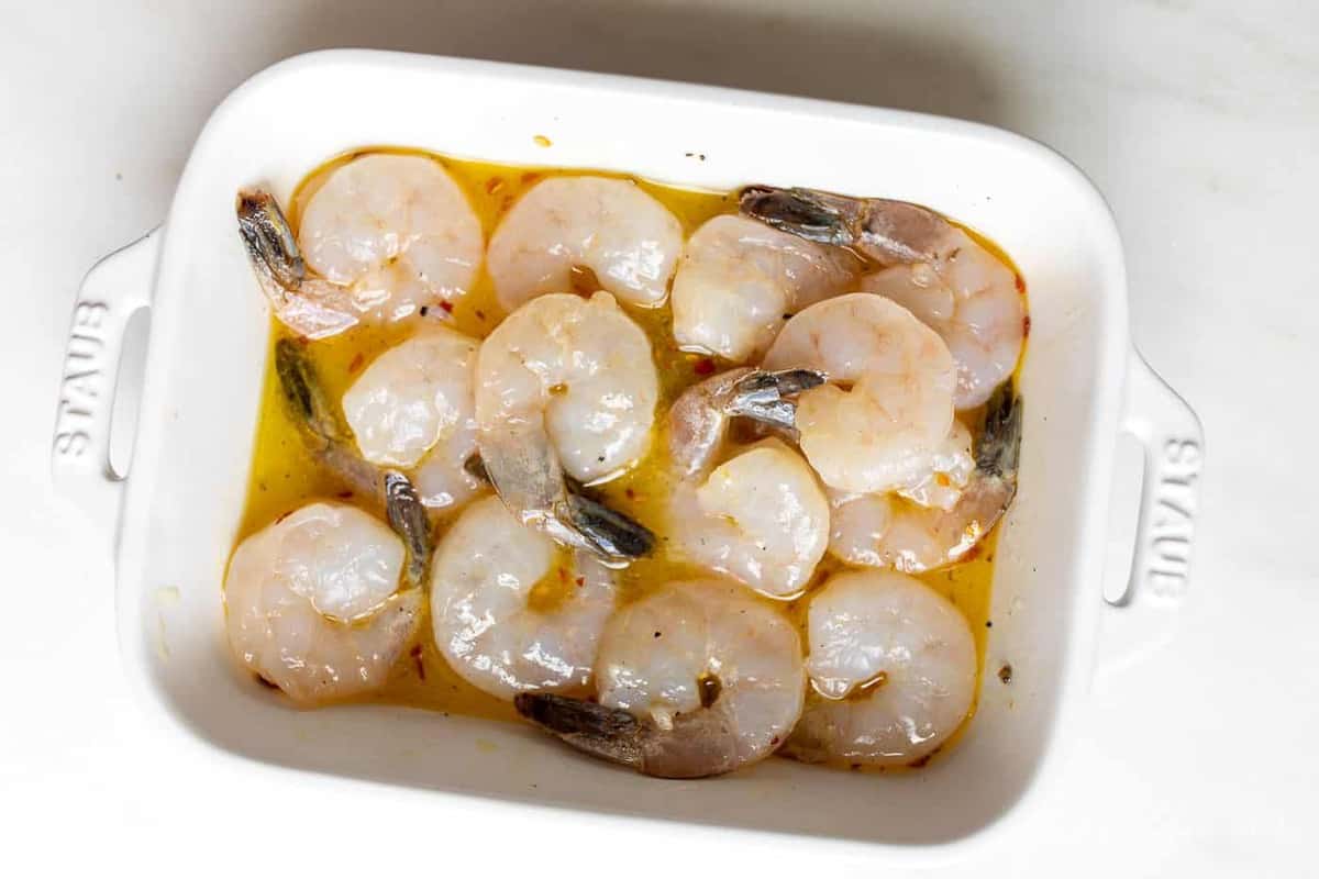 A white dish with marinating tequila lime shrimp for grilled shrimp skewers.