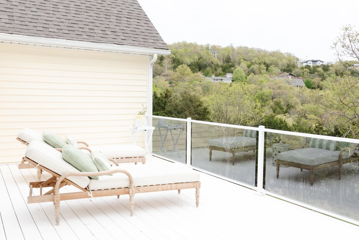 Outdoor deck with two cushioned lounge chairs, a small table, glass railing, and a scenic view of trees and hills in the background, all elevated by durable vinyl decking.