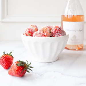Drunken strawberries covered in sugar, in a white bowl, for a 4th of July recipe.