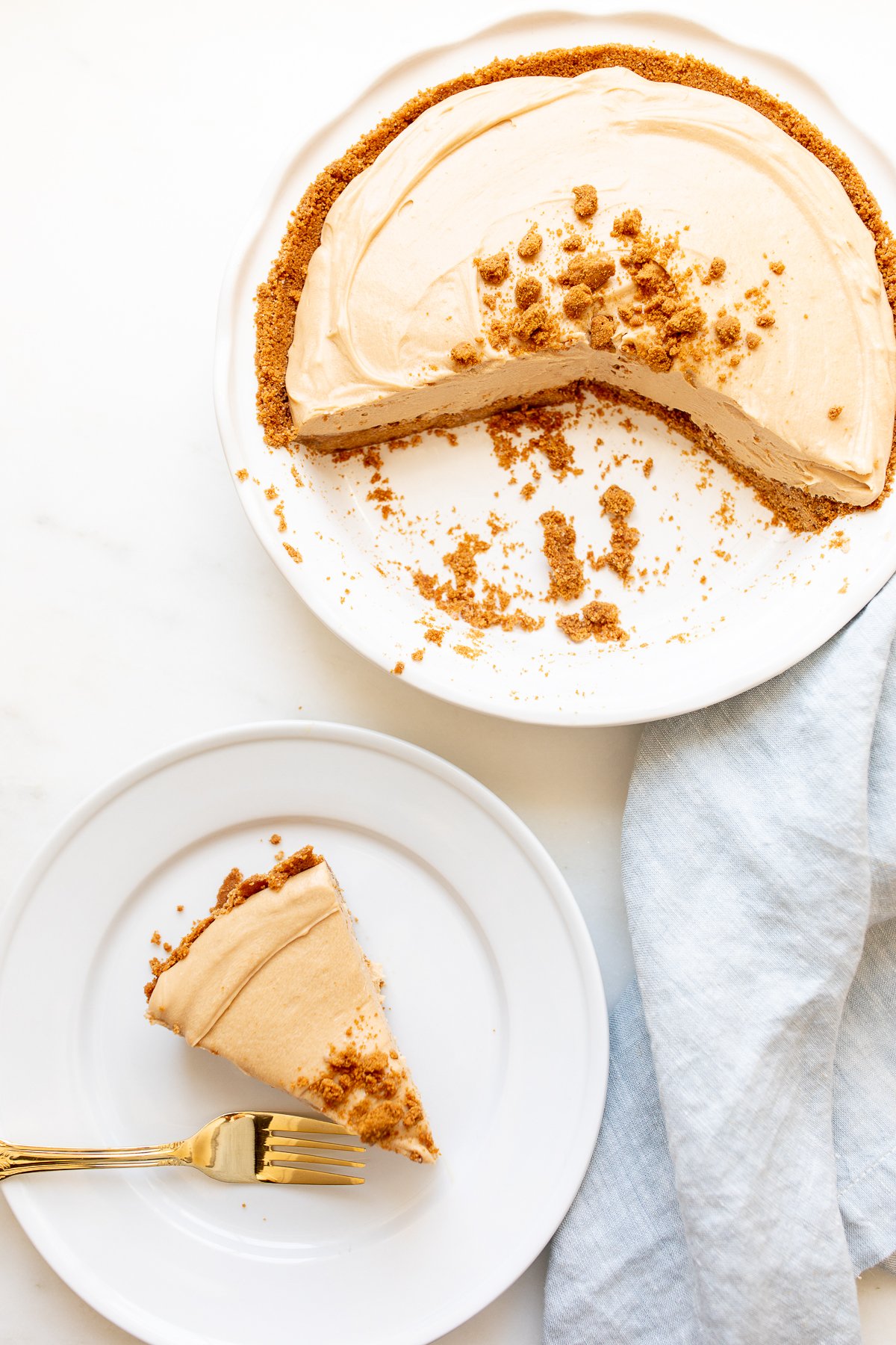 A slice of no bake cookie butter cheesecake on a white plate, with a pie pan behind it.