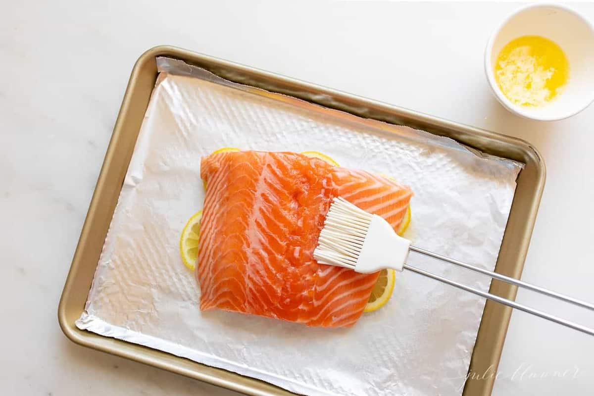 A single fillet of lemon pepper salmon on a foil lined aluminum sheet.