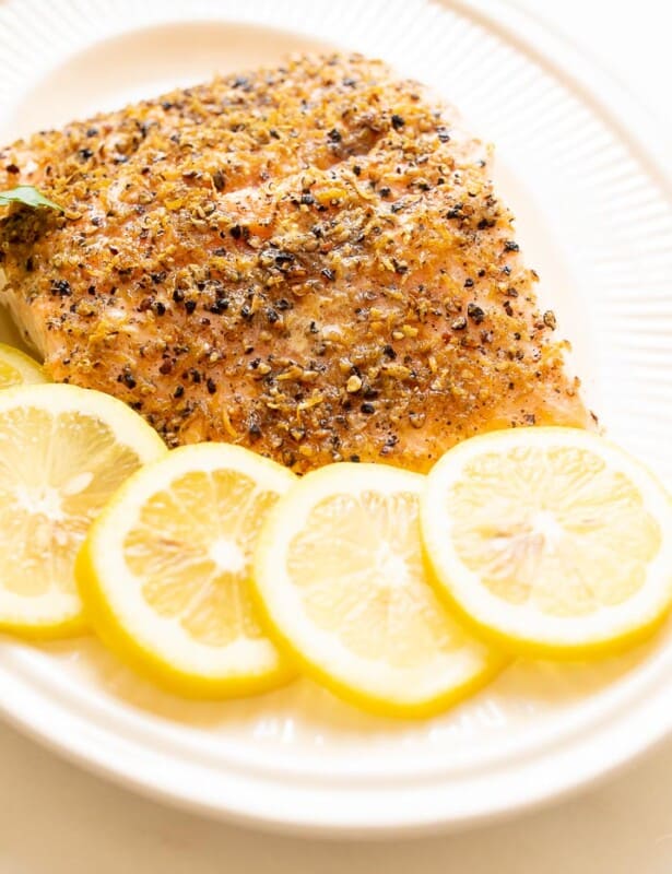 A white oval platter featuring a fillet of lemon pepper salmon, sliced lemons on the side.