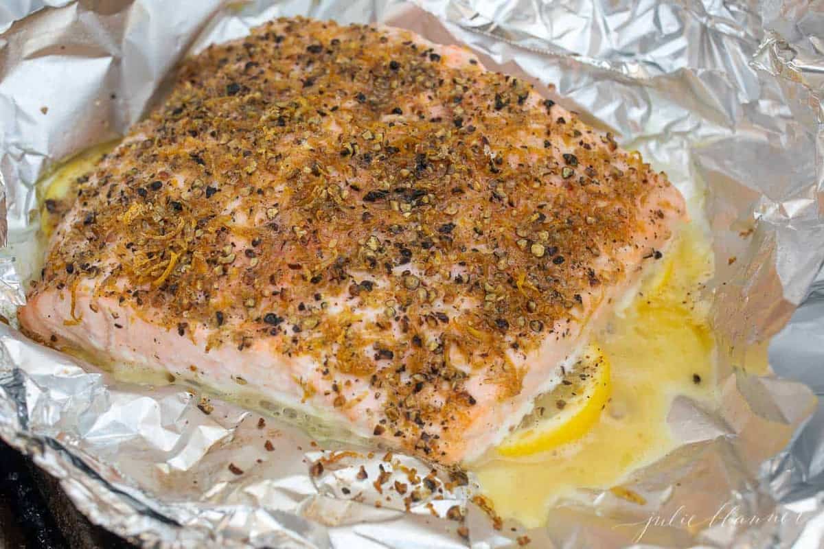 A single fillet of lemon pepper salmon on a foil lined aluminum sheet.