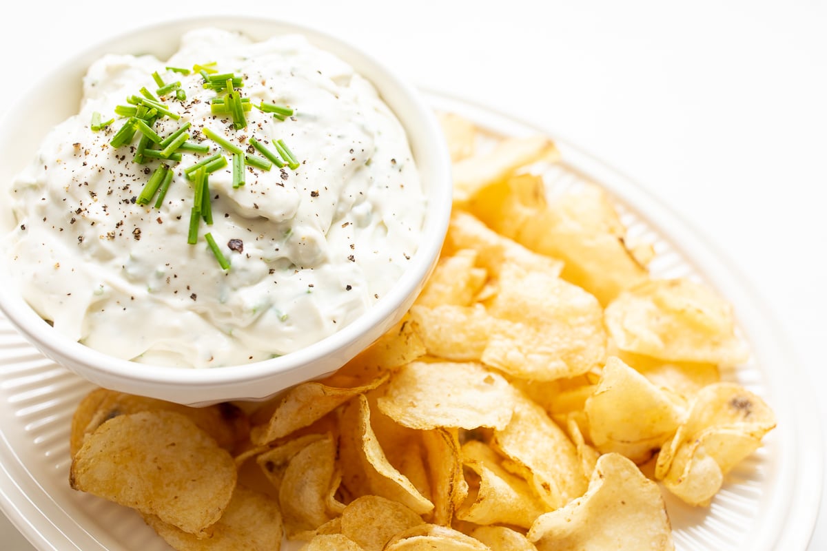 blue cheese dip in a white bowl, on a platter of potato chips.
