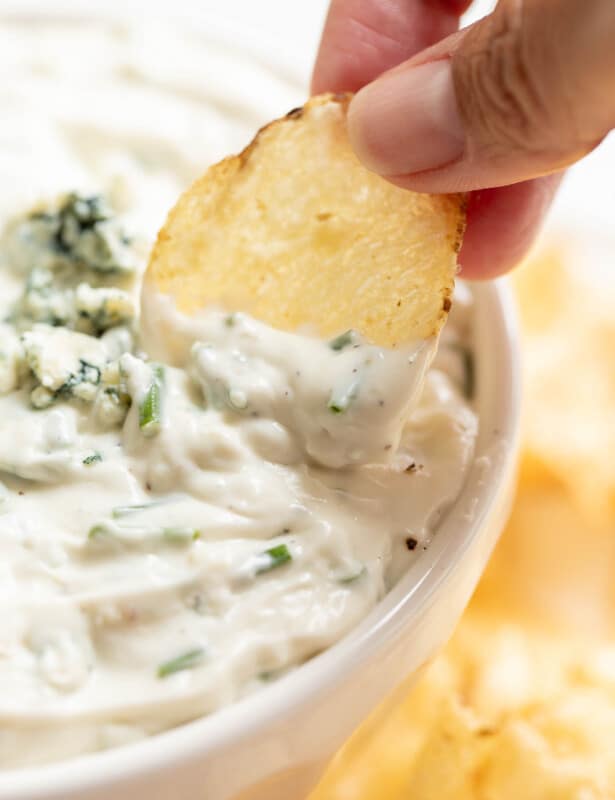 dipping chip into blue cheese dip in white bowl