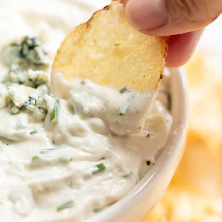 dipping chip into blue cheese dip in white bowl