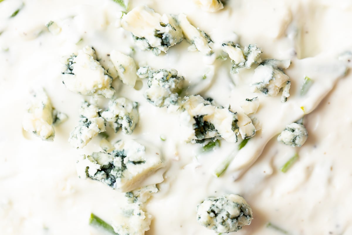 A close up of blue cheese crumbles in a bowl of dip.
