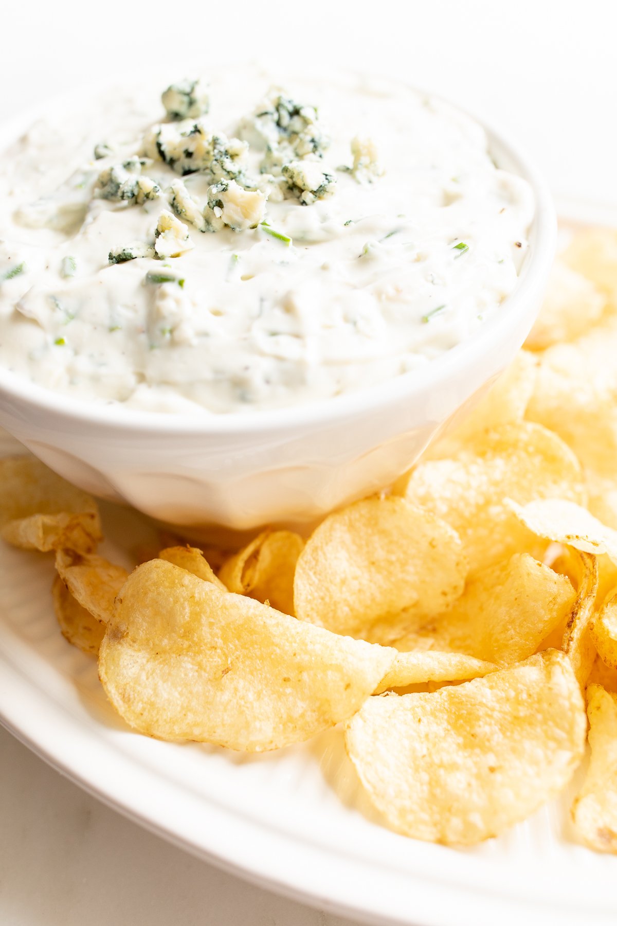 blue cheese dip in a white bowl, on a platter of potato chips.