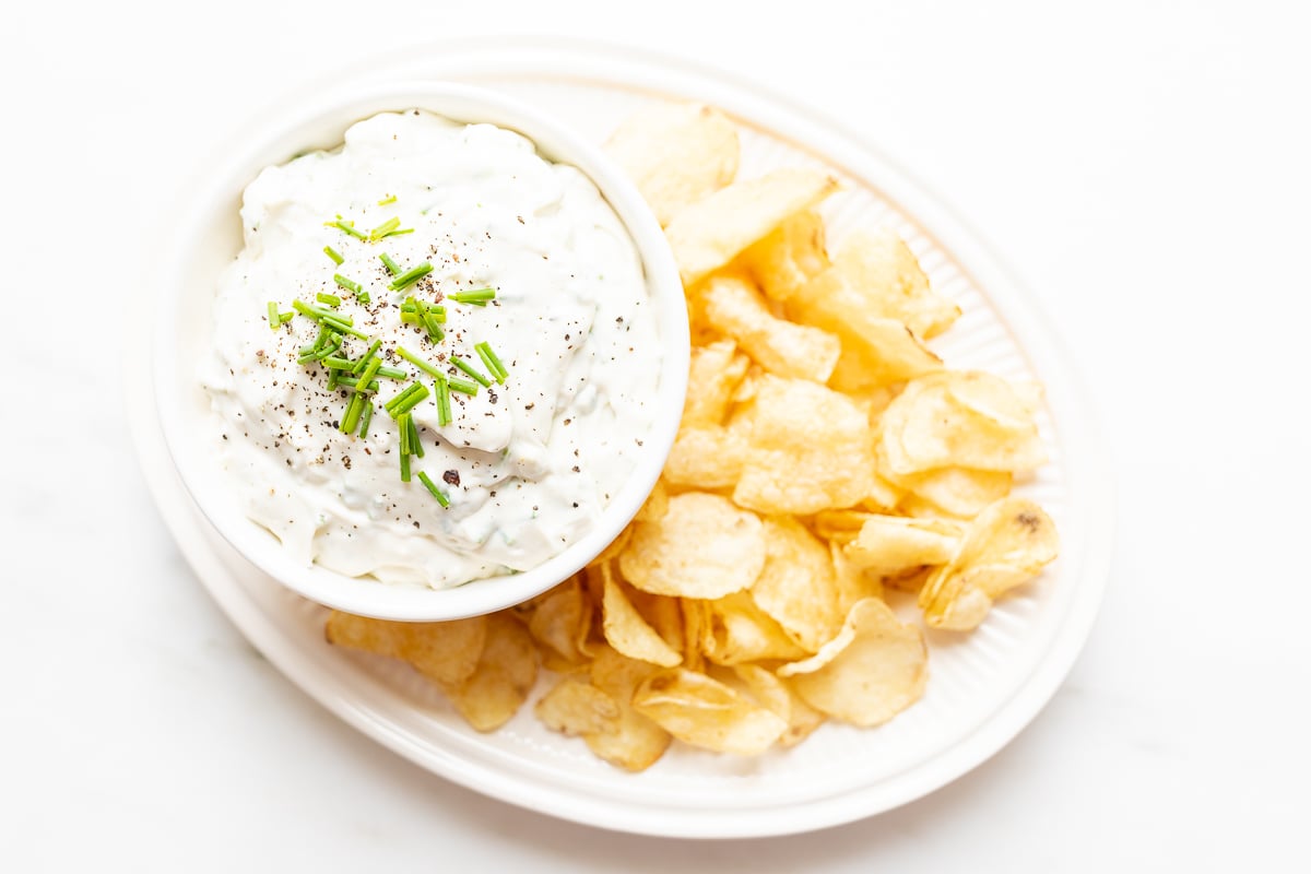blue cheese dip in a white bowl, on a platter of potato chips. 