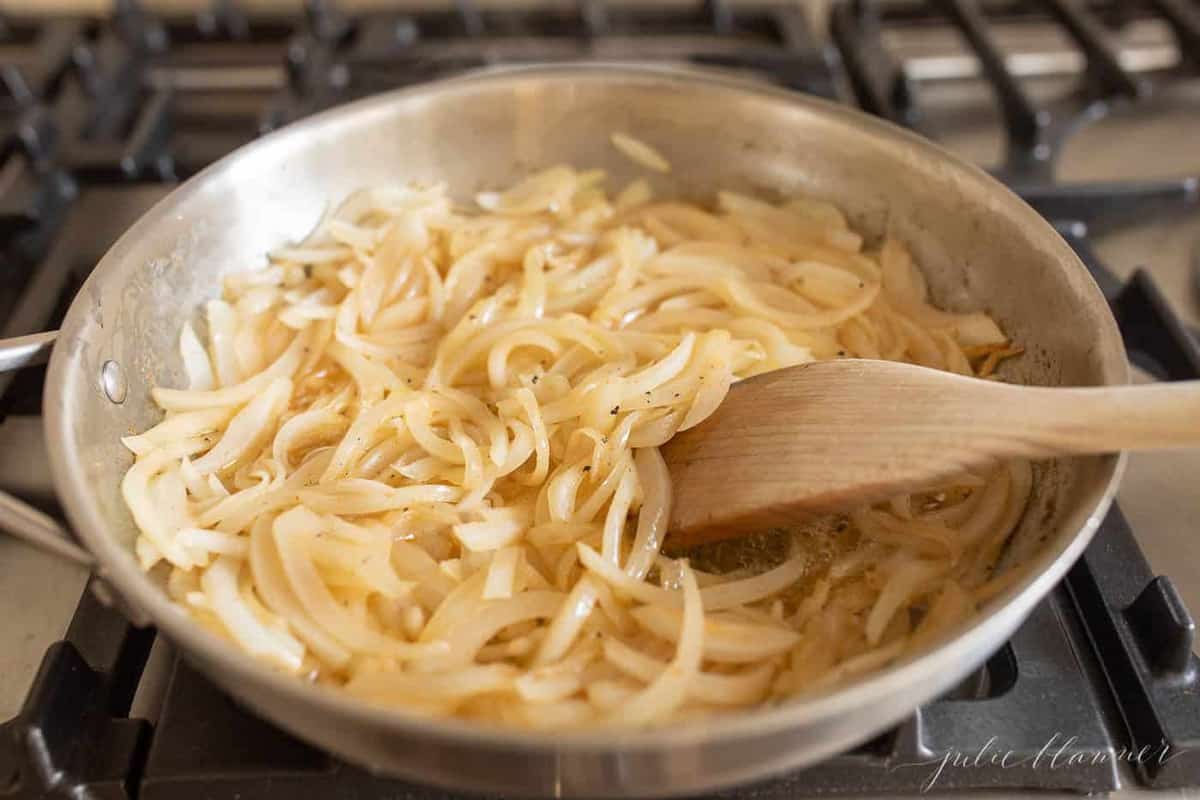 Skillet on stovetop with sliced onions and wooden spoon