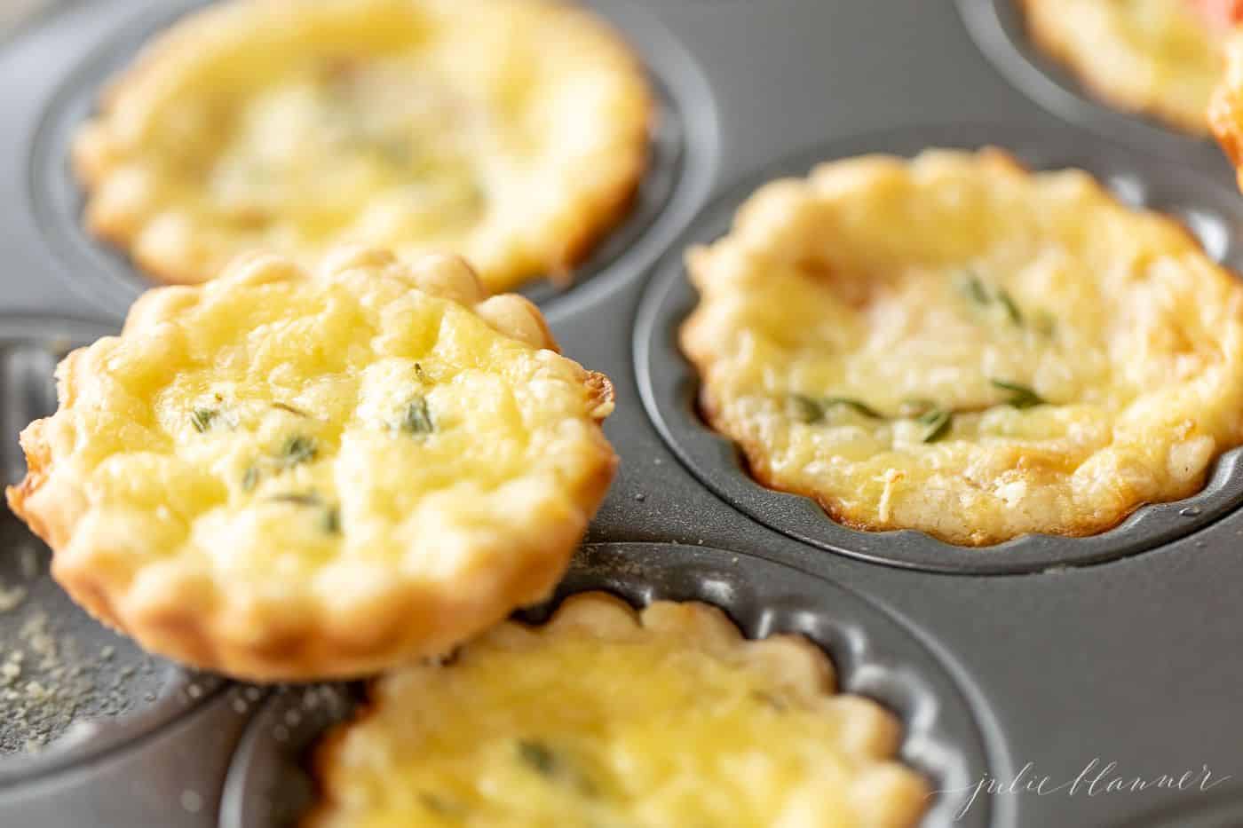A muffin pan with cheddar cheese tarts in each cup.