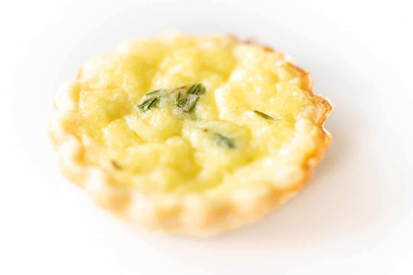 A small cheddar cheese tart topped with fresh herbs on a marble surface.