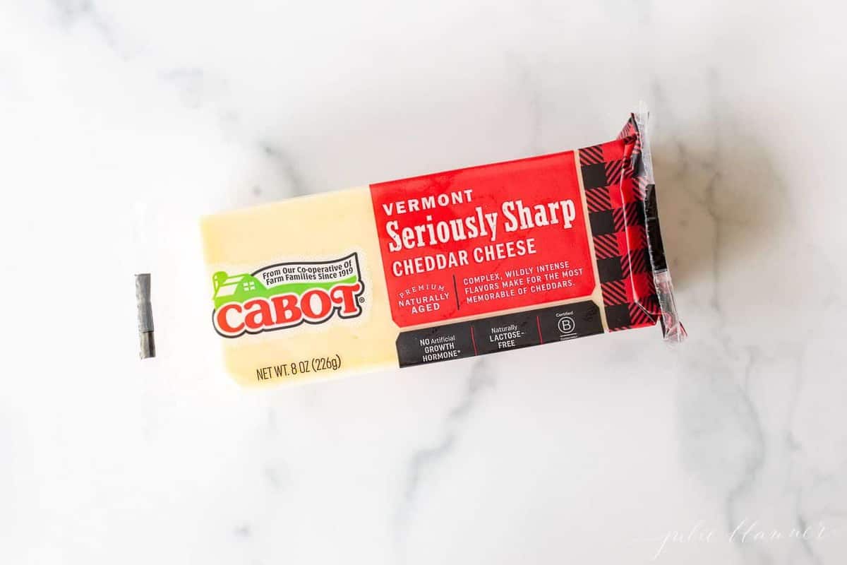 A white marble surface with a packaged block of Cabot sharp cheddar cheese.