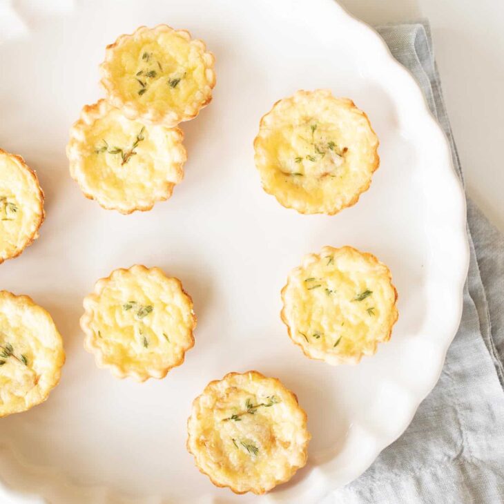 A white scalloped dish filled with small cheddar cheese tarts.