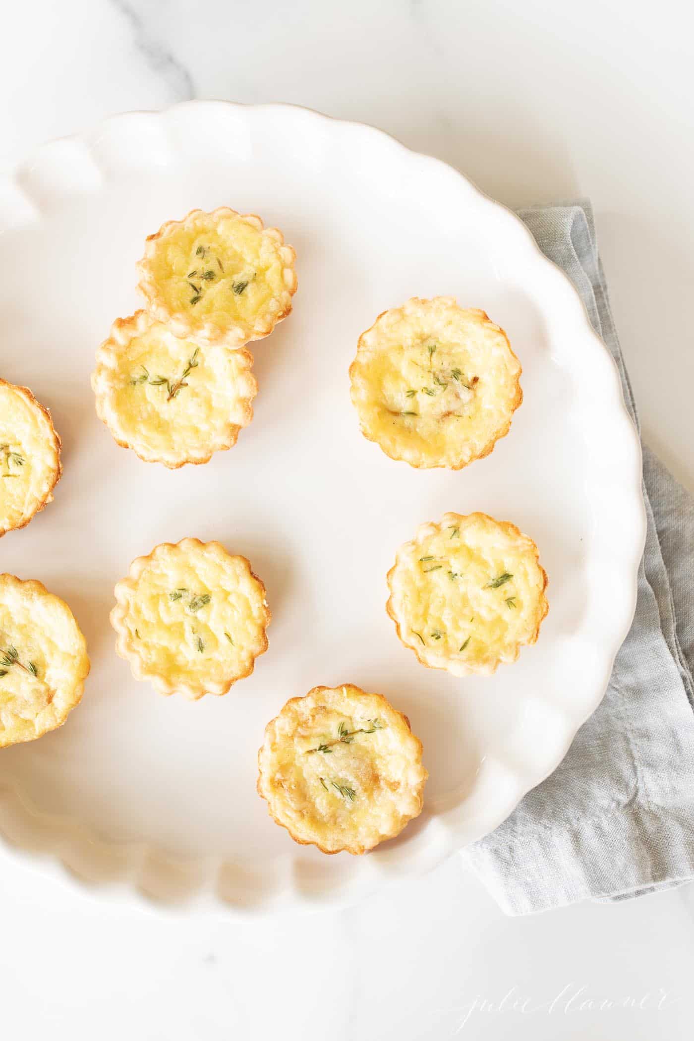 A white scalloped dish filled with small cheddar cheese tarts.