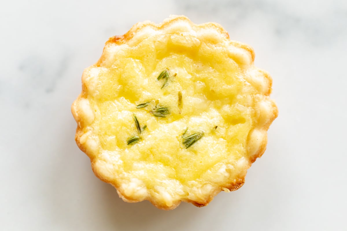 A single mini cheese tart with a cream cheese crust on a marble countertop.