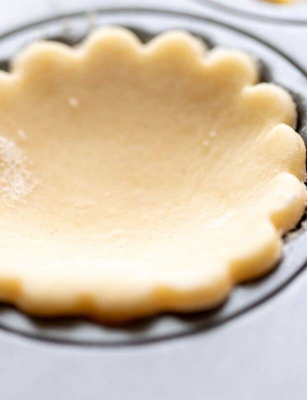 A scalloped cream cheese pie crust cut out, resting in a muffin tin.