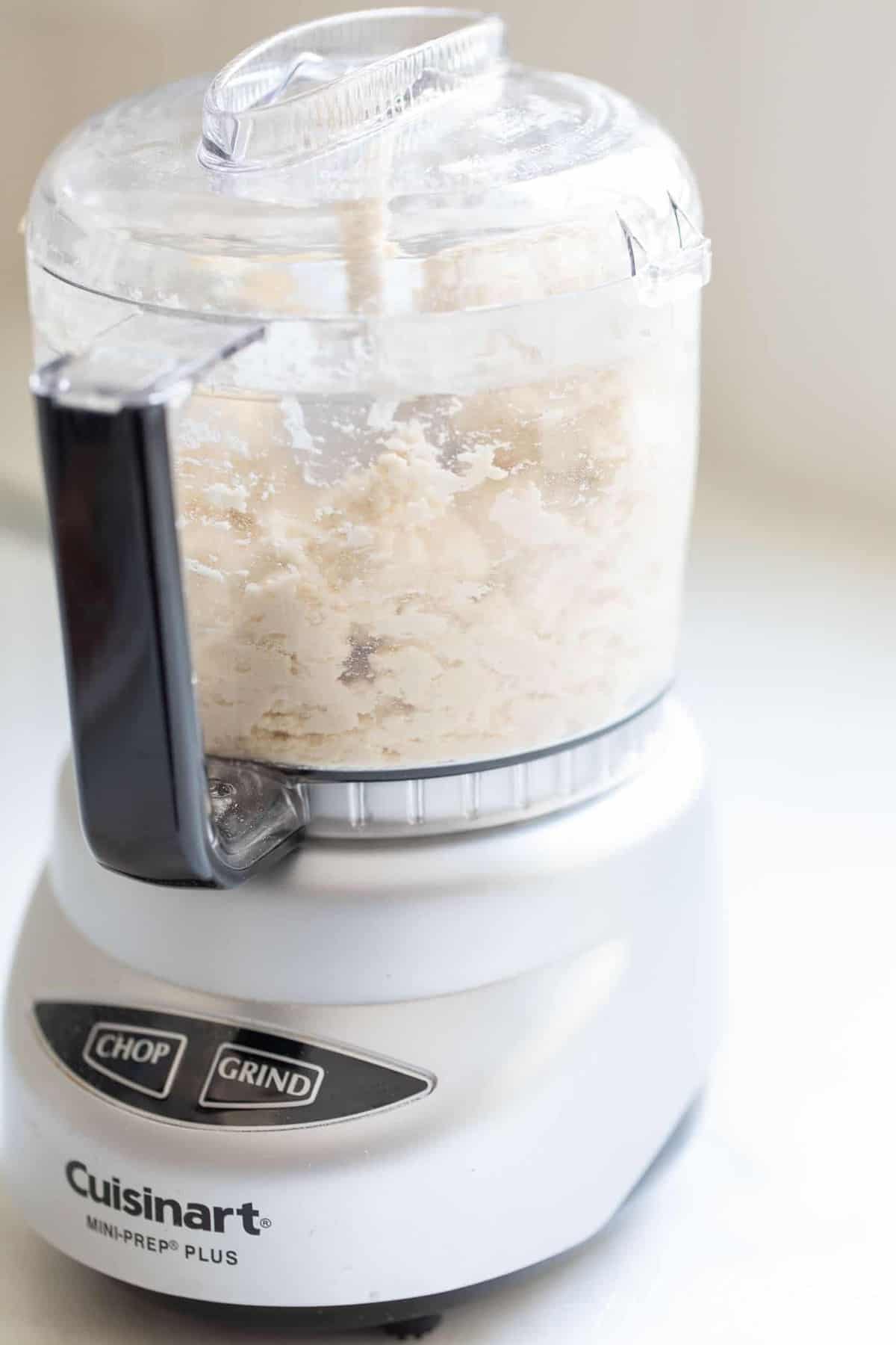 A food processor filled with the ingredients for a cream cheese pie crust.