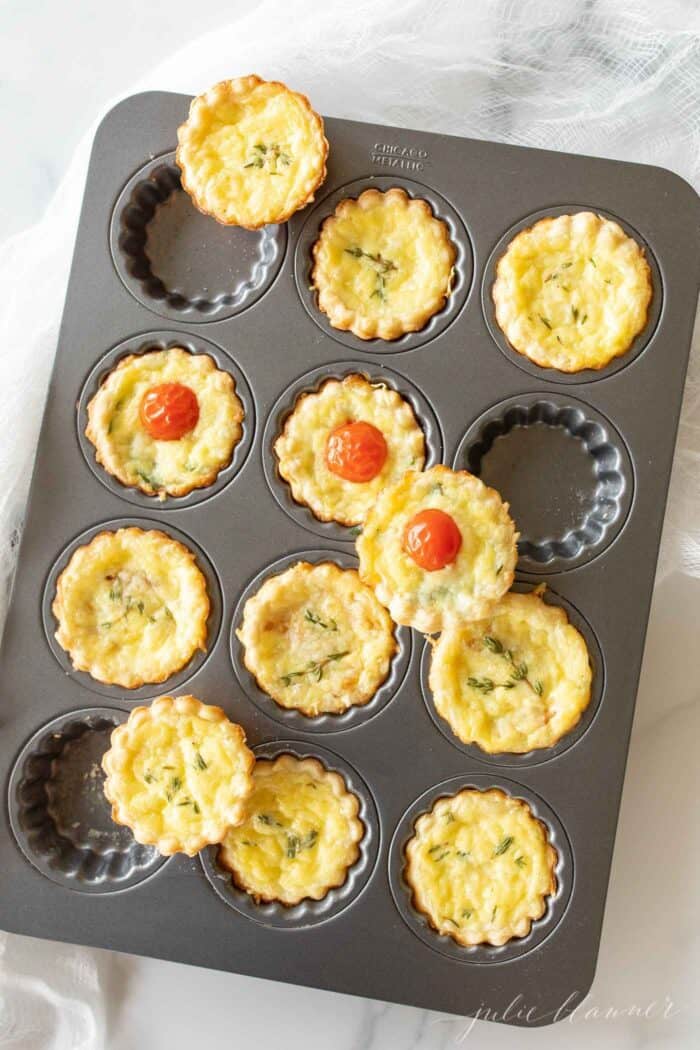 A metal tart pan with small cheese tarts with a cream cheese pie crust recipe as the scalloped edges.