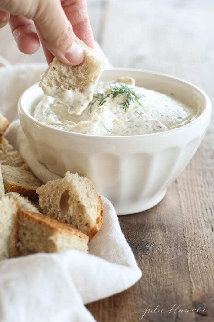 A hand reaching into a white bowl full of dill dip.