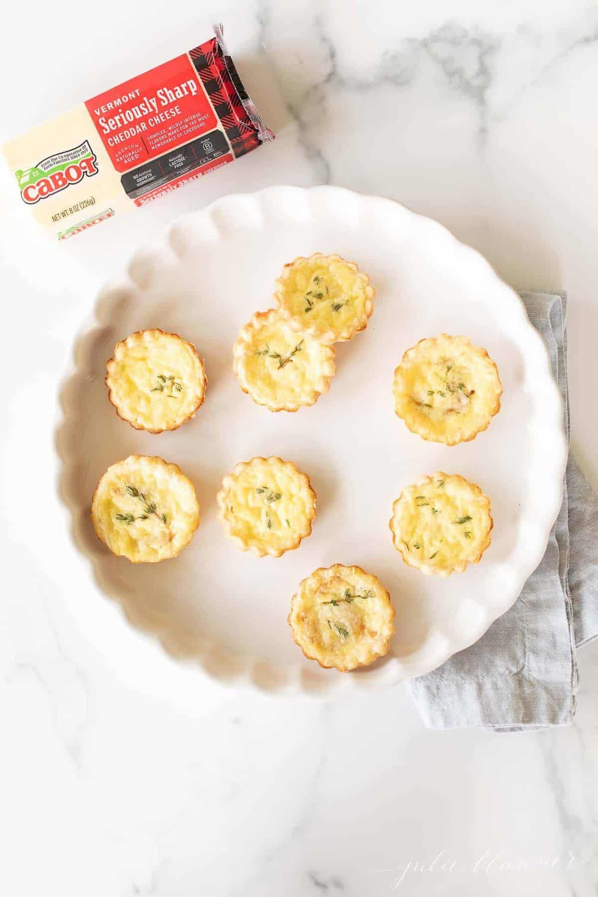 A white scalloped dish filled with small cheddar cheese tarts.