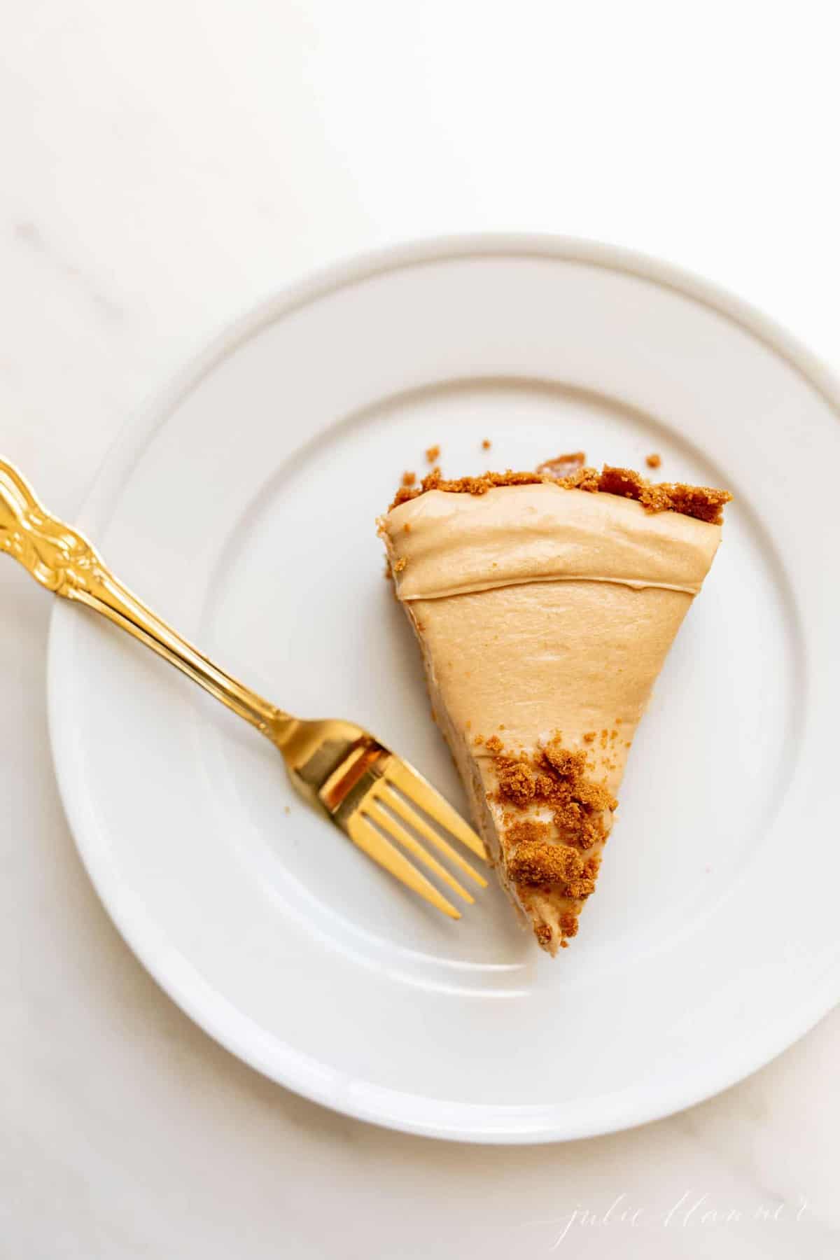 A white plate with gold fork to the side of a slice of no bake cookie butter cheesecake.