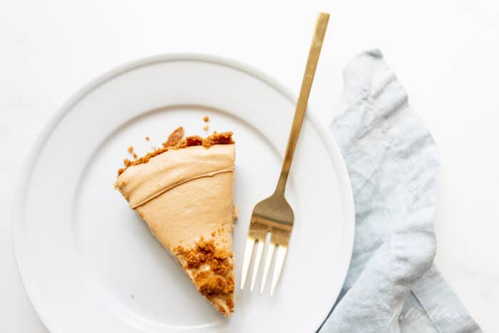 A white plate with gold fork to the side of a slice of cookie butter cheesecake.
