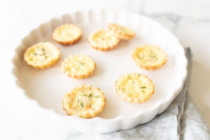 A round white scalloped serving platter filled with mini cheese tarts in an easy cream cheese pie crust.