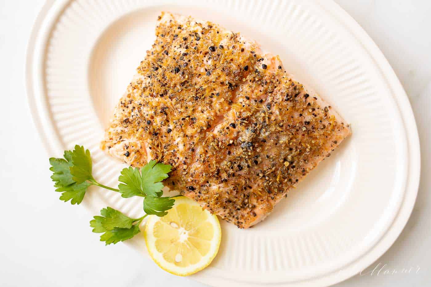 Lemon pepper salmon on a white oval platter with sliced lemon to the side.