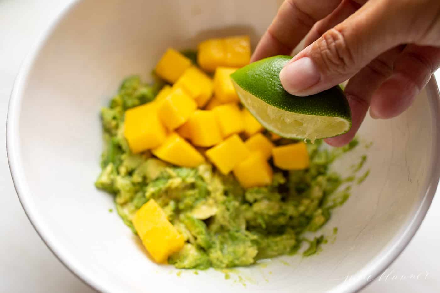 A bowl of mango guacamole with lime being squirted on top