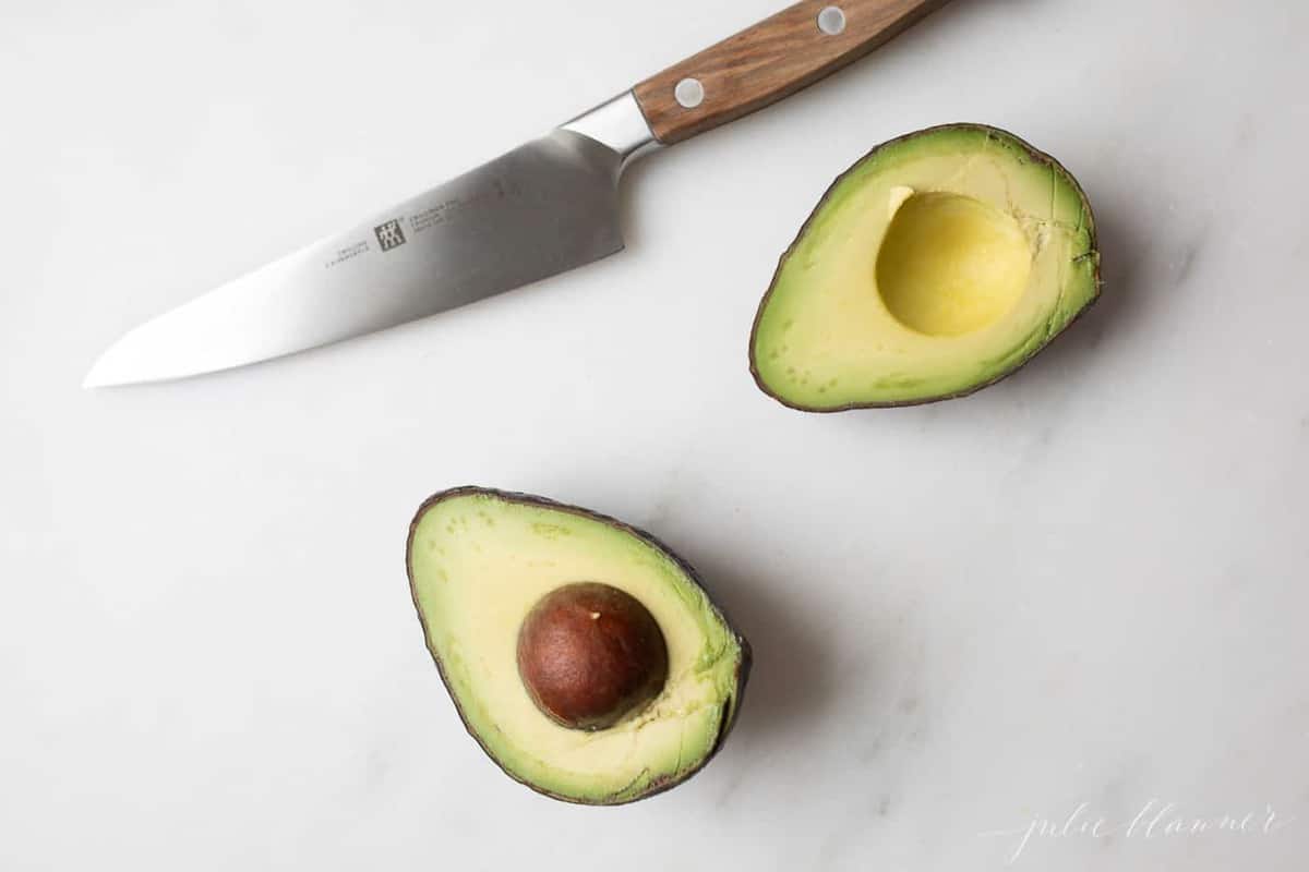 An avocado cut in half with a knife to the side
