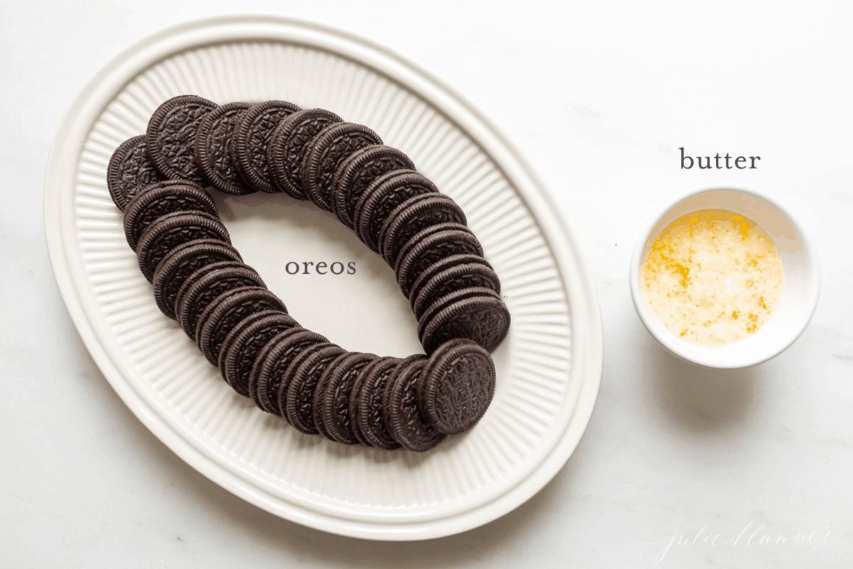 White platter full of oreos and a white ramekin full of melted butter for ingredients to make an oreo cookie pie crust recipe.