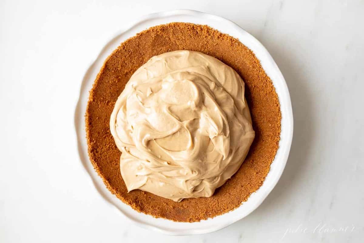 A white pie pan full of speculoos cookie crust with a no bake cookie butter cheesecake filling.
