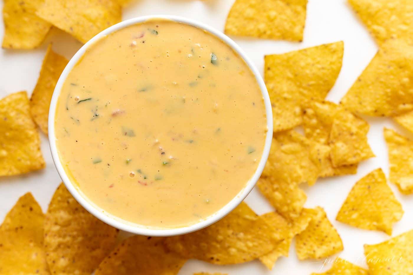 A white bowl full of cheese dip surrounded by tortilla chips.