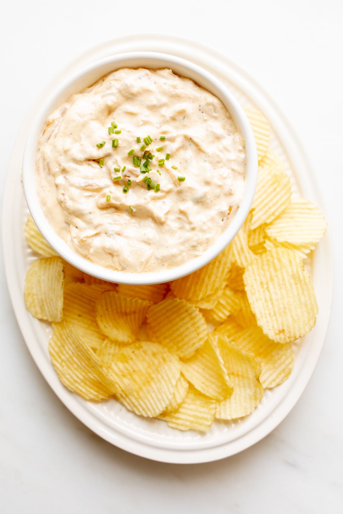 A bowl full of homemade french onion dip, surrounded by potato chips.
