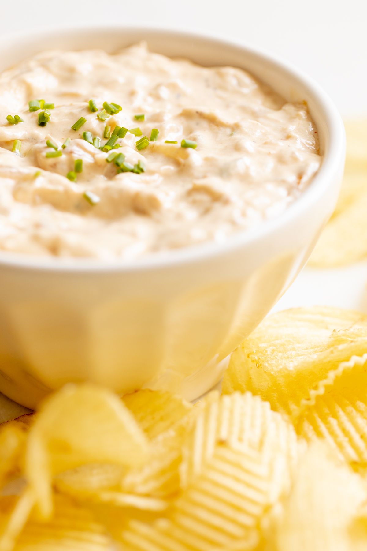 A bowl full of homemade french onion dip, surrounded by potato chips.